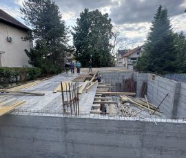 Construction site with foundation and workers under cloudy sky.